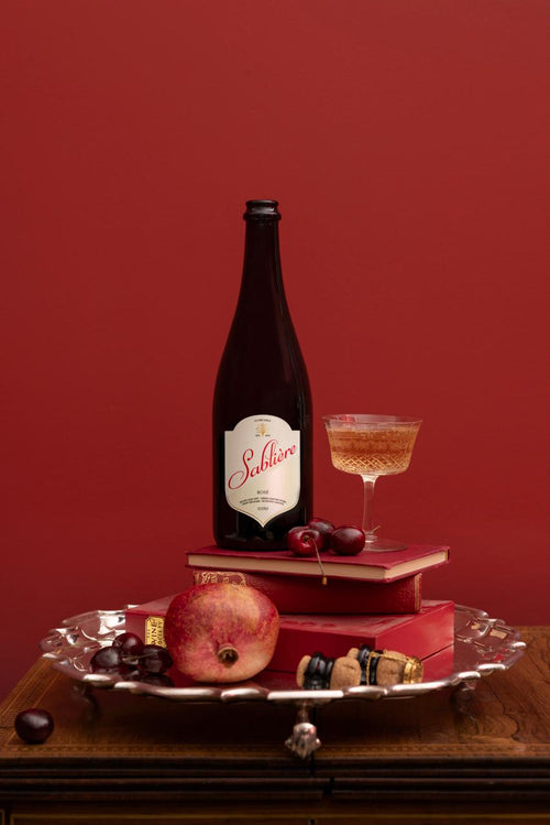 Bottle of Sabliere with a glass on a decorative tray against a red background